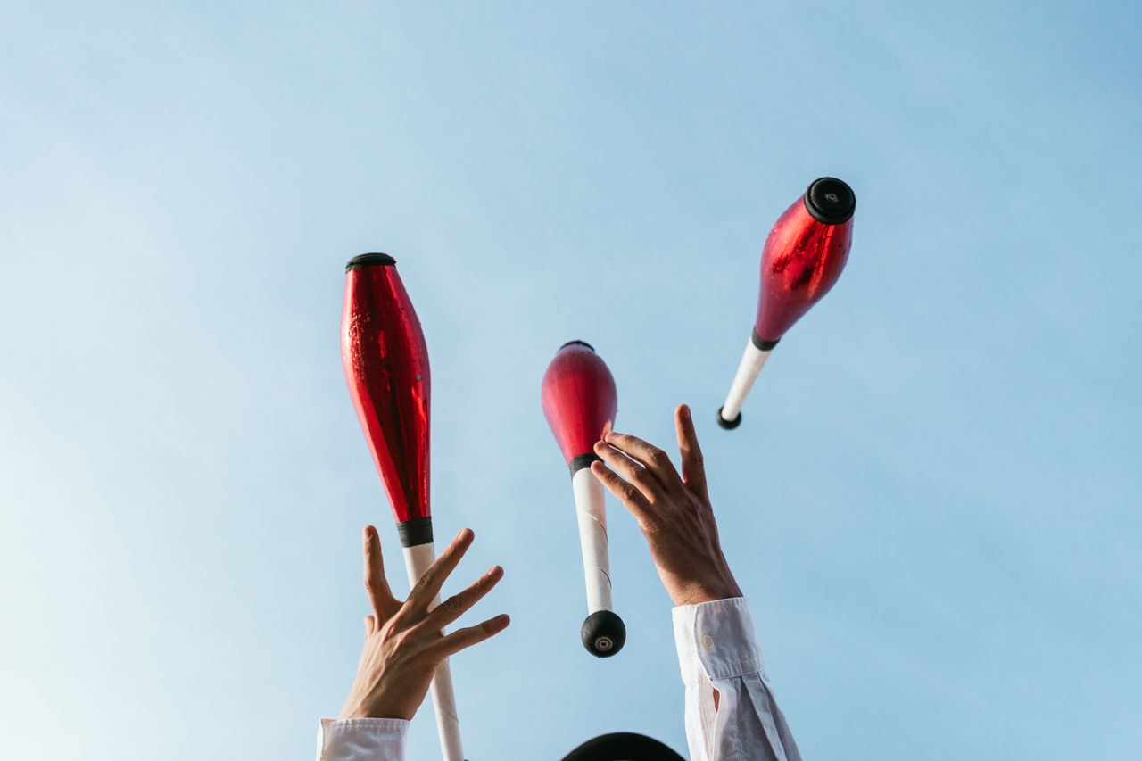 From below of crop anonymous circus artist performing trick with juggling clubs against blue sky; Shutterstock ID 2023786334; purchase_order: Masterbrand - Loop 4; job: ; client: ; other: 